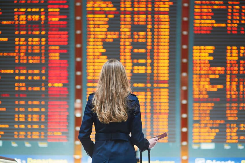 Femme aux cheveux longs consultant un tableau d'affichage de vols à l'aéroport avant de voyager au Canada