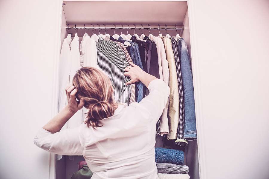 Une femme examine sa garde-robe remplie de vêtements variés, illustrant une collection prêt-à-porter femme adaptée à tous les styles