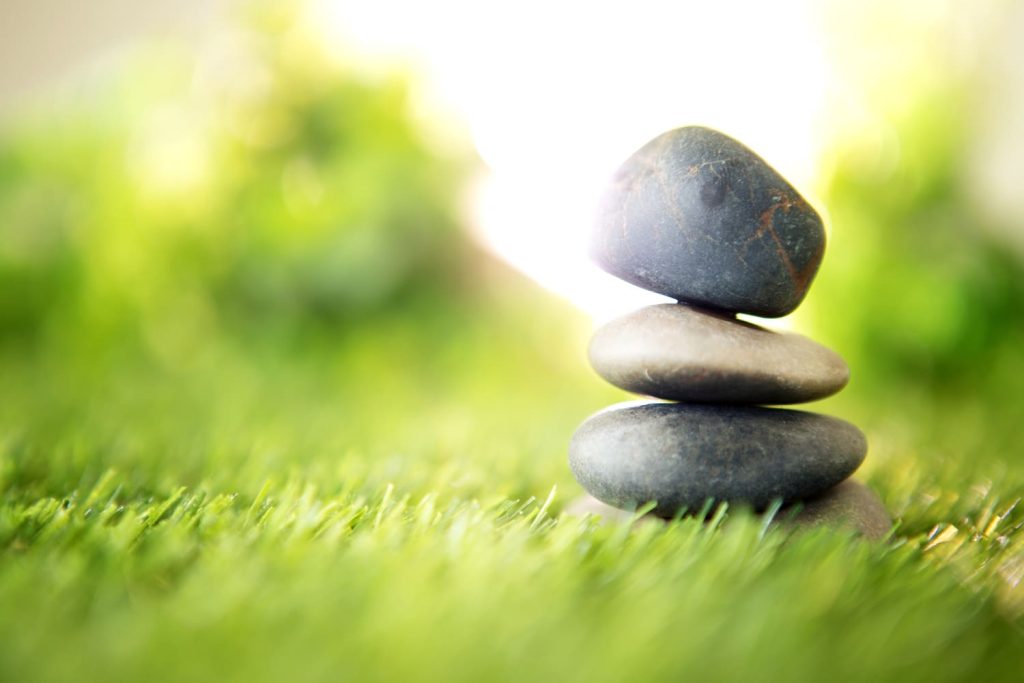 Trois pierres lisses empilées en équilibre sur herbe verte, symbolisant le lien entre forme, rythme et perception