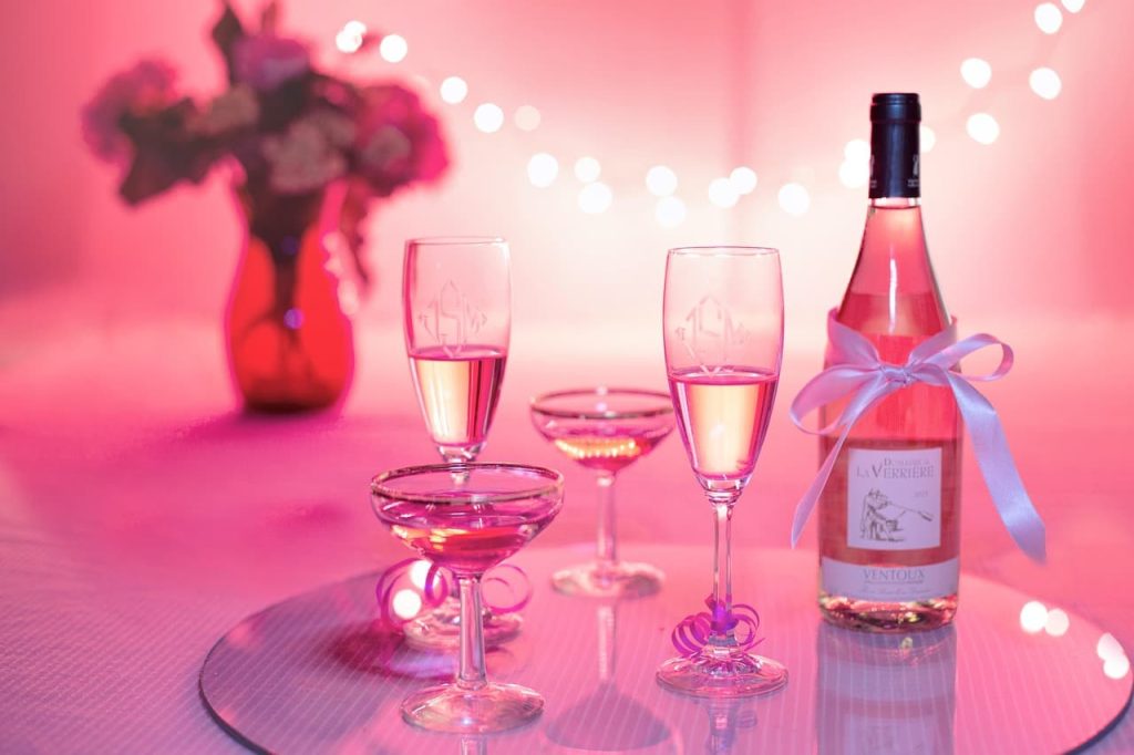 Bouteille de vin rosé avec ruban blanc accompagnée de verres élégants sur plateau miroir dans une ambiance romantique rose
