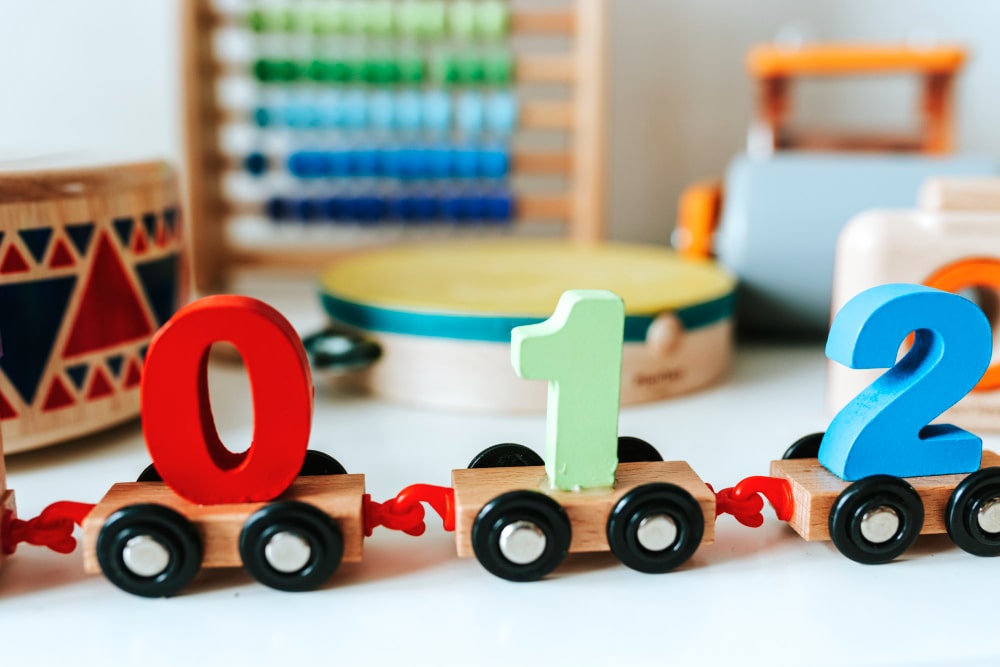Gros plan sur un train de chiffres en bois colorés, accompagné d'un boulier et d'un tambour, illustrant l'importance des jouets éducatifs pour enfants