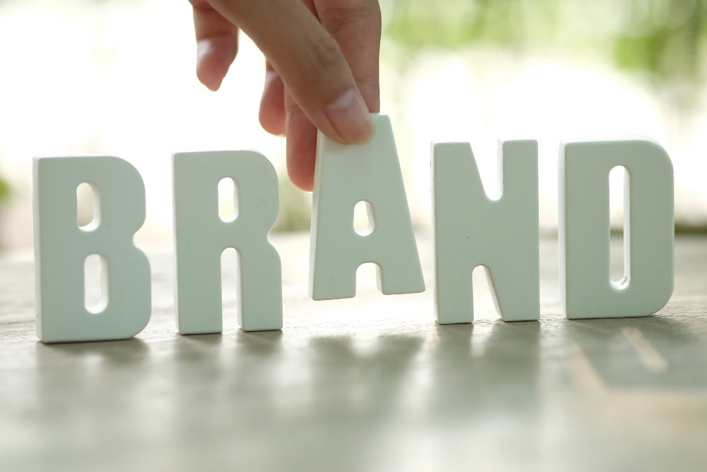 Une main place la lettre "A" dans le mot "BRAND", symbolisant la construction et la protection d'une marque via le droit des marques