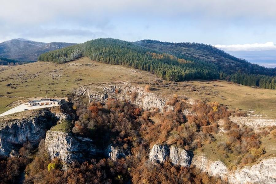 Falaises rocheuses et forêts de pins surplombant un Balkan landscape aux couleurs automnales.