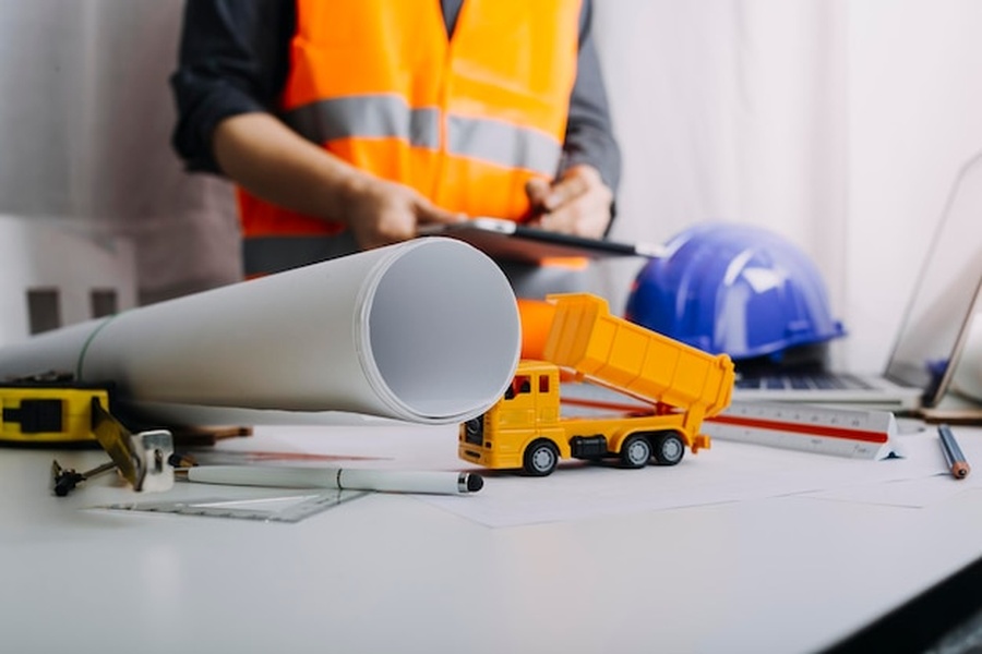 Un professionnel examine les plans d'un projet de construction entouré d'outils de mesure et d'un casque de sécurité.