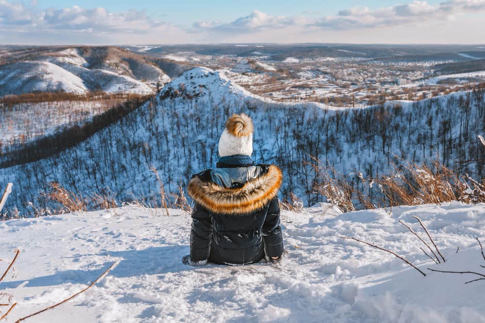 Voyageuse de dos admirant un vaste paysage de montagnes enneigées lors d'une coolcation en Scandinavie
