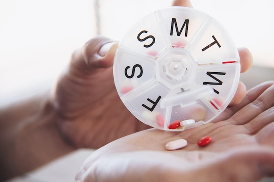 Une main tenant un pilulier circulaire blanc pour organiser une cure basée sur les bienfaits du magnésium bisglycinate pour le sommeil et l'anxiété : le guide expert.