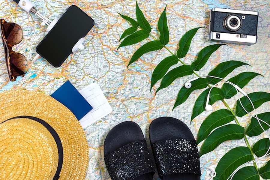 Accessoires de voyage comme un chapeau de paille, un appareil photo et des lunettes disposés sur une carte pour une Coolcation : les meilleures destinations secrètes pour voyager au frais cet été.