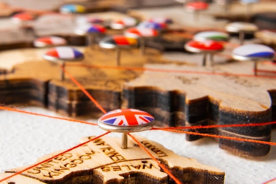 Une carte du monde en bois parsemée de punaises drapeaux pour identifier des Destination Dupes : les alternatives moins chères et moins fréquentées aux lieux touristiques saturés.