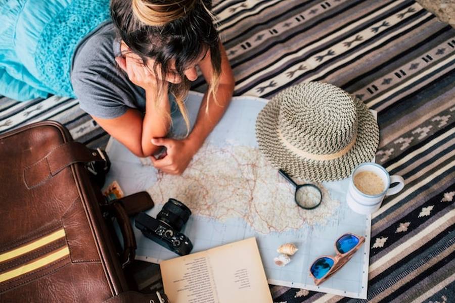 Une voyageuse examine une carte du monde à la recherche de Destinations Dupes : Les meilleures alternatives abordables pour éviter le surtourisme.