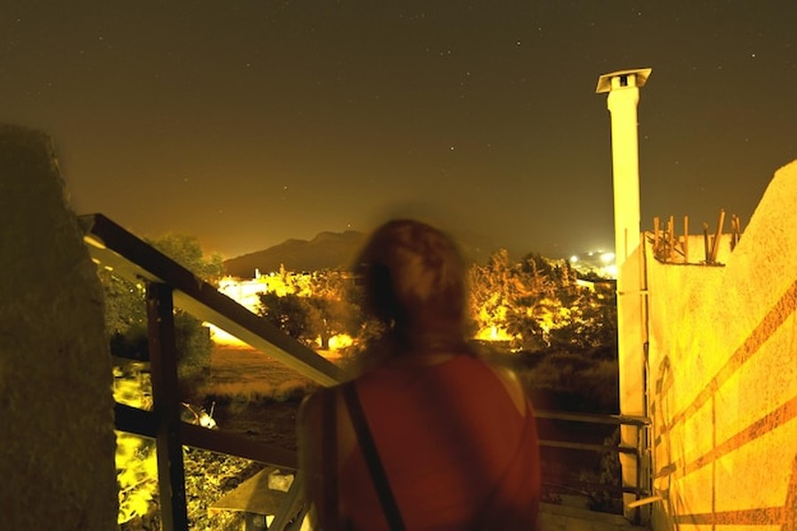 Une voyageuse admire le ciel étoilé au-dessus d'un paysage montagneux, suivant les recommandations du Guide de l'astro-tourisme : Les meilleures destinations pour observer les étoiles loin de la pollution lumineuse.