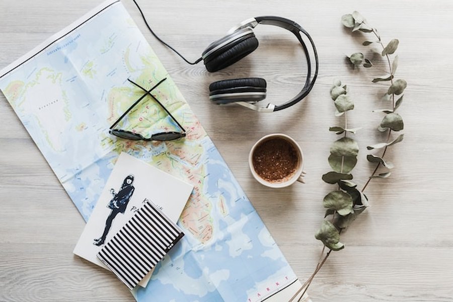 Une carte du monde, un casque audio et une tasse de café disposés sur un bureau en bois pour organiser un Silent Travel : comment identifier et choisir les destinations sans pollution sonore pour se ressourcer.