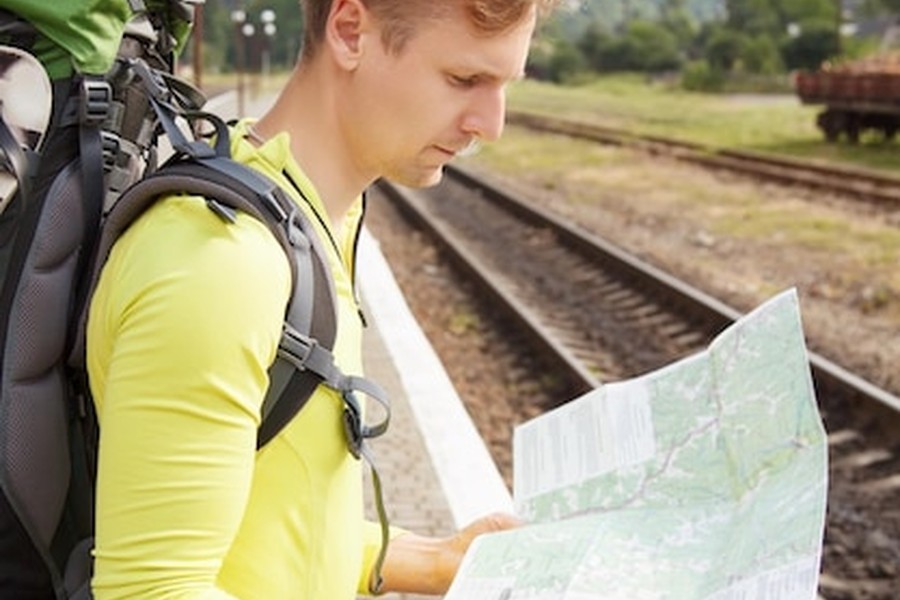 Un voyageur avec un sac à dos examine attentivement une carte sur un quai de gare, une étape clé de ce Guide complet pour voyager en train en Ouzbékistan : itinéraire sur la Route de la Soie.