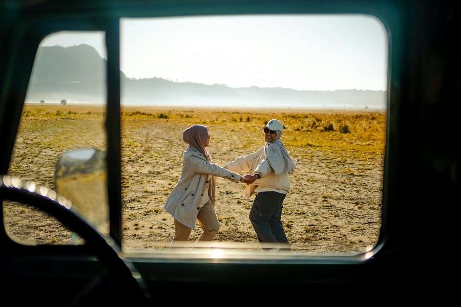 Deux femmes se tenant la main dans un paysage aride et ensoleillé vu depuis une voiture, parfait pour voyager hors saison.