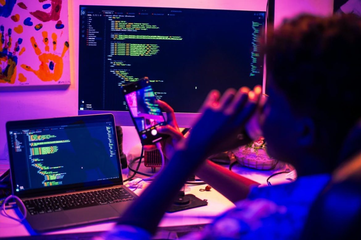 Un développeur travaille sur plusieurs écrans affichant du code informatique dans une ambiance tamisée, idéal pour apprendre à débuter avec IA.