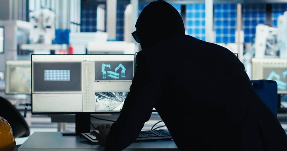 Un individu en silhouette devant des écrans de contrôle industriels illustrant les risques de la fuite de données et la cyberattaque dans une usine connectée.