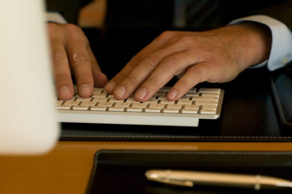Mains d'un professionnel en costume tapant sur un clavier d'ordinateur de bureau, illustrant l'externalisation de la saisie de données.