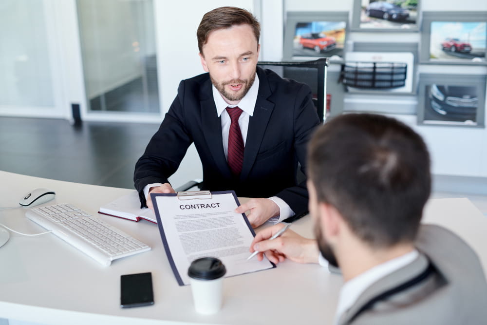 Un professionnel de l'automobile présentant un contrat à signer sur un bureau, idéal pour illustrer les démarches de création d'entreprise et l'utilisation de monidenum demande kbis.