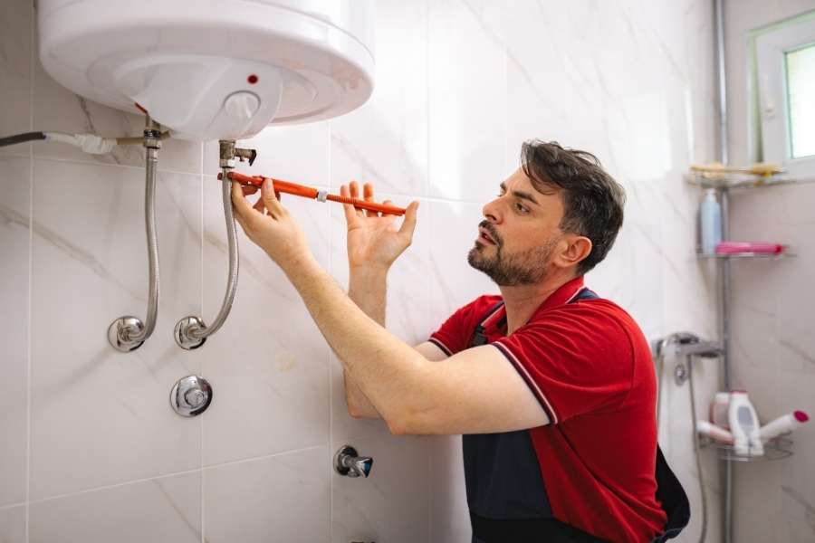 Un plombier répare un chauffe-eau qui fuit dans une salle de bain carrelée.