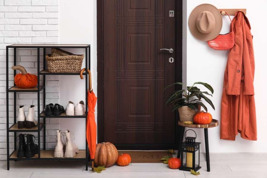Entrée décorée pour l'automne avec un bloc-porte en bois sombre et un meuble à chaussures.