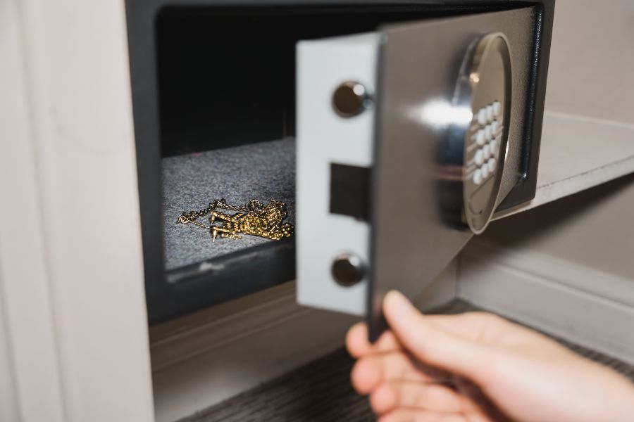 Une main ouvrant la porte d'un petit coffre-fort de maison contenant une chaîne en or, idéale pour comprendre comment choisir un coffre-fort domestique ignifuge.